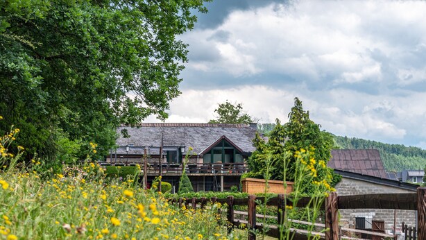 A rustic house with a wooden deck, surrounded by lush greenery and a wooden fence. - Hotel Ulftaler Schenke (Burg-Reuland)