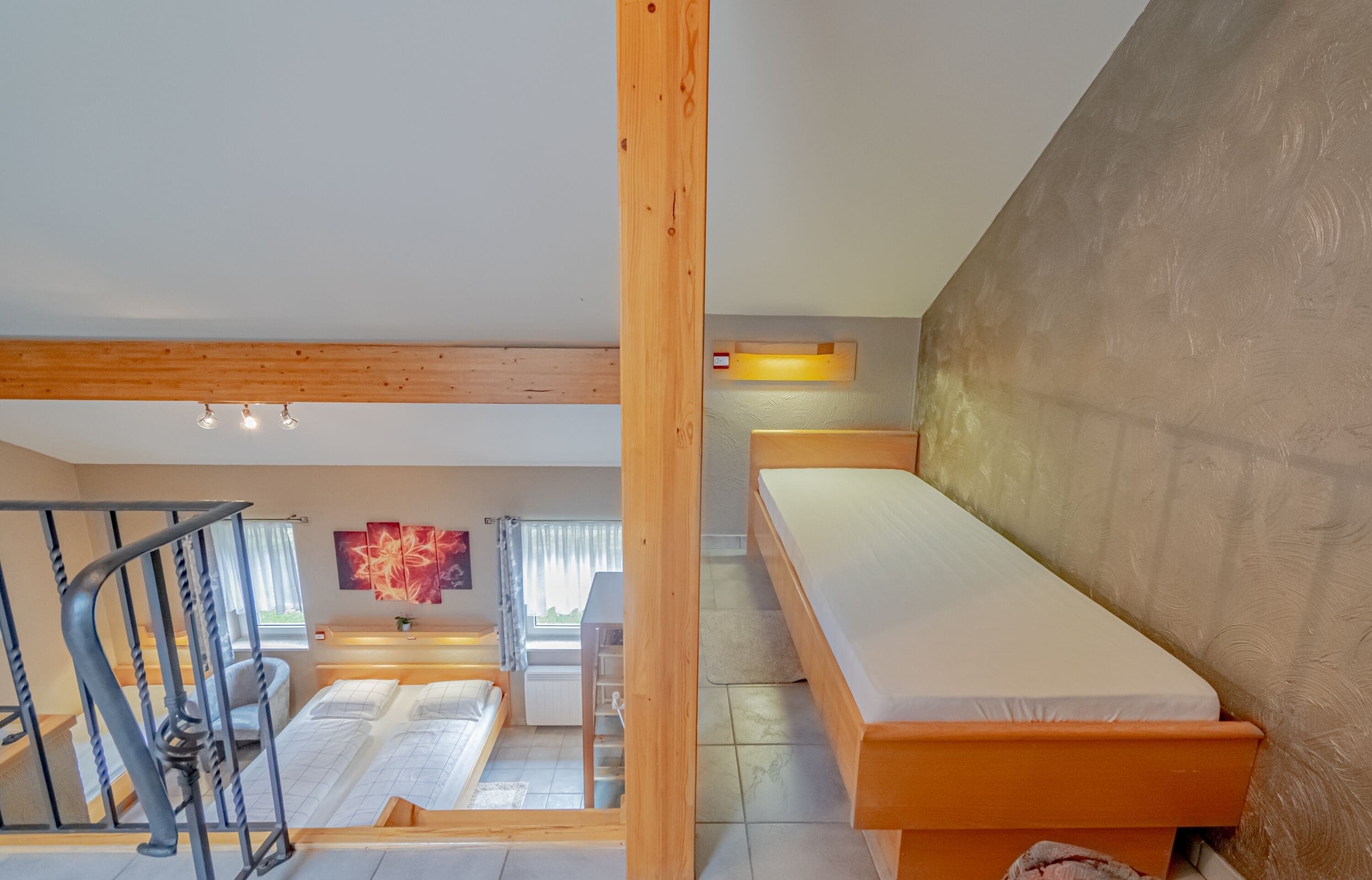 A modern loft-style bedroom with a large bed, a wooden headboard, and a staircase leading to an upper level.