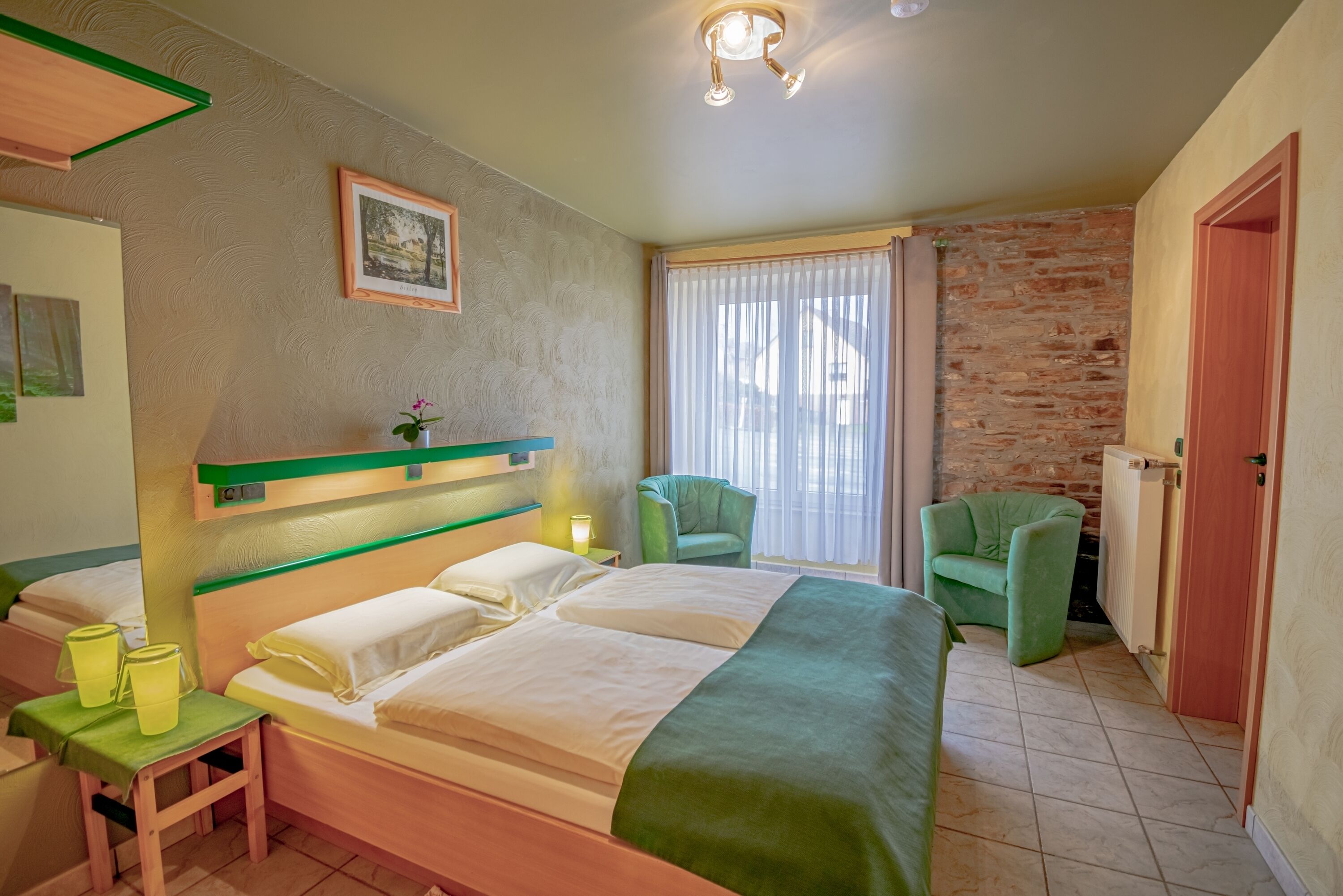 Een hotelkamer met een bed, een stoel, een klein tafeltje, een radiator en een raam met gordijnen.