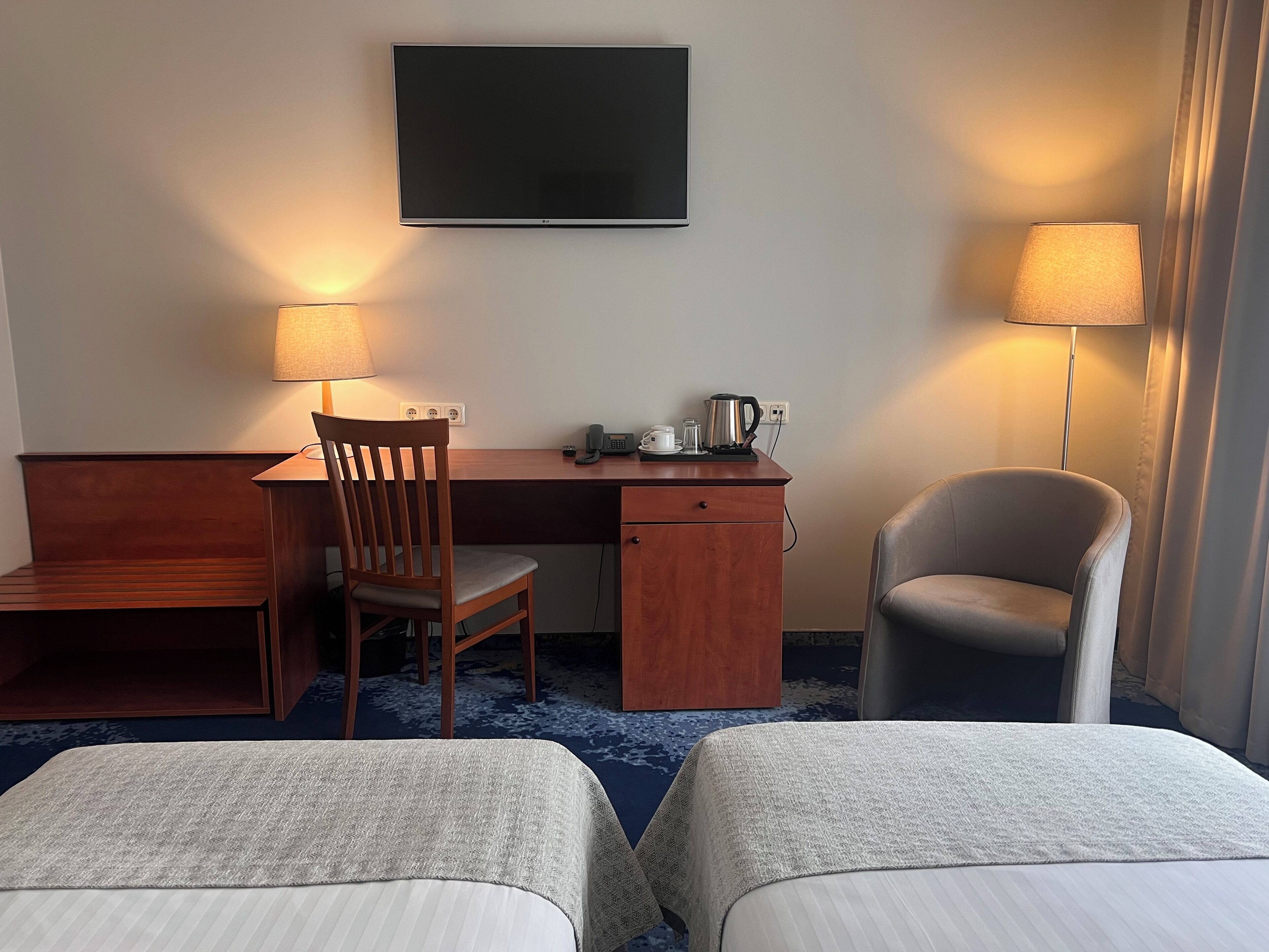 Una habitación de hotel con escritorio, dos sillas, televisor y lámpara.