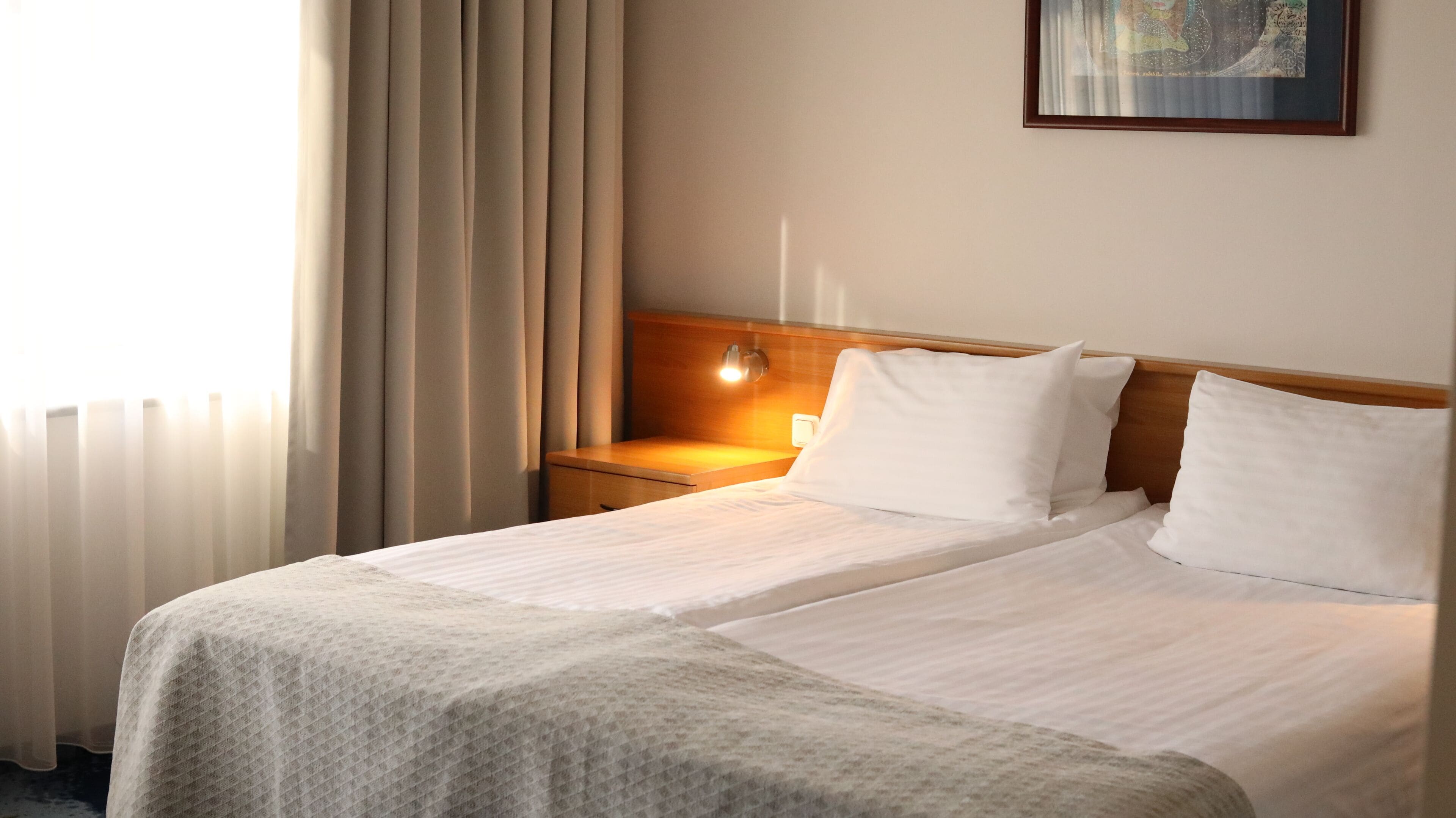 A hotel room with a bed, a nightstand, a wall-mounted lamp, and a painting on the wall.