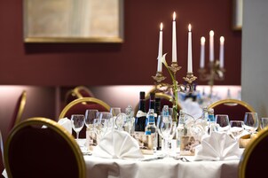 Una mesa de comedor con manteles blancos, sillas doradas y velas encendidas.