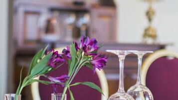 Una mesa de comedor con jarrones de vidrio transparente que contienen flores moradas, una mesa de madera y una lámpara de araña al fondo.