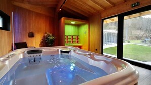Een hottub in een houten ruimte met uitzicht op een grasveld.
