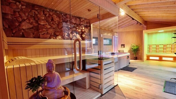 Een wellnessruimte met een stenen muur, een Boeddhabeeld, een massagetafel en een houten vloer.