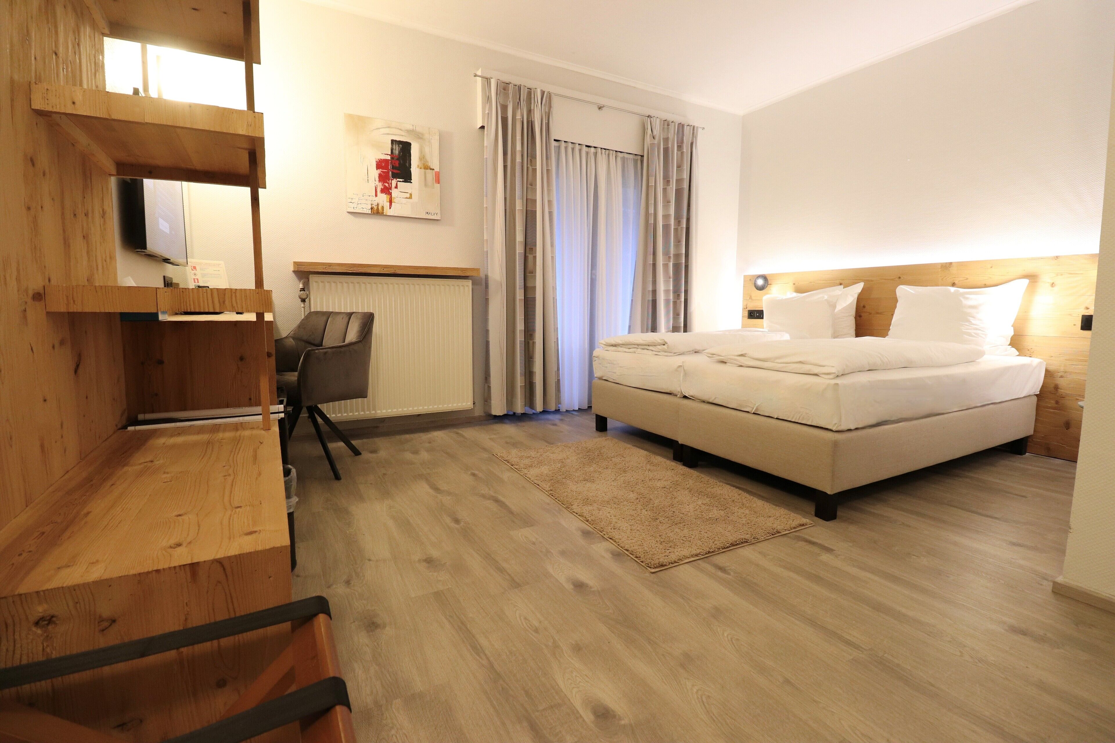 A bedroom with a bed, a desk, a chair, a radiator, and curtains.