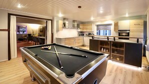 Een moderne woonkamer met een pooltafel, een eethoek en een keuken.