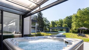 Een whirlpool met glazen omheining, een zwembad en een overdekt terras.