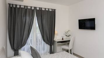 Un dormitorio con cama, escritorio, silla, televisor y ventana con cortinas.