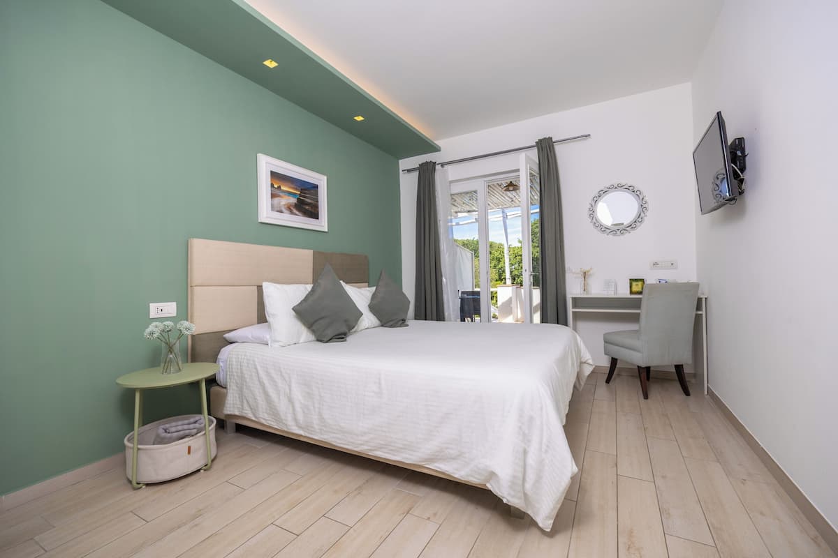 A bedroom with a bed, bedside table, chair, desk, and a TV.