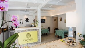 Un vestíbulo de hotel con una recepción, un área de comedor y un televisor instalado en la pared.