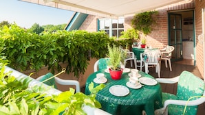 A covered patio with a table set for dining, surrounded by potted plants and white chairs. - Hotel Garni Schneevoigt (Hagenburg)
