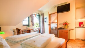 A bedroom with two beds, a desk, a chair, a TV, and a kitchenette. - Hotel Garni Schneevoigt (Hagenburg)