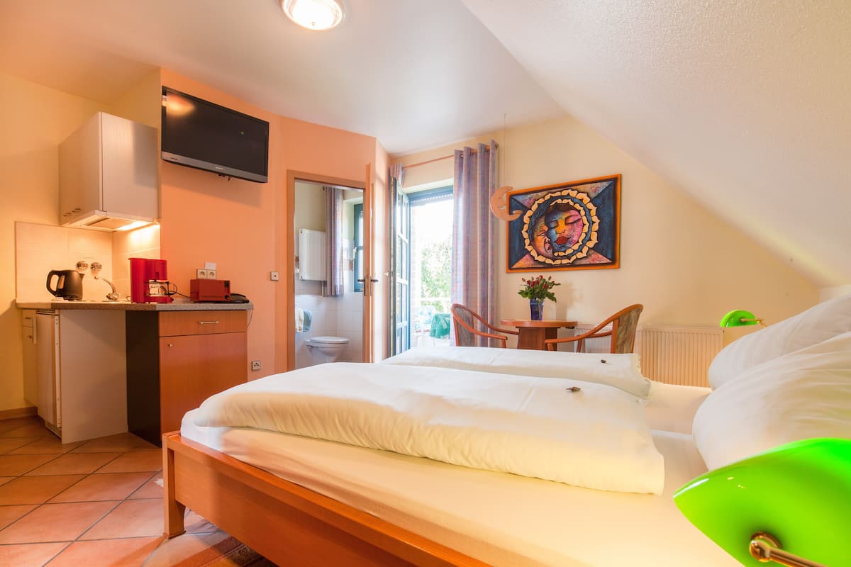 A bedroom with a bed, a desk, a chair, a television, and a painting.