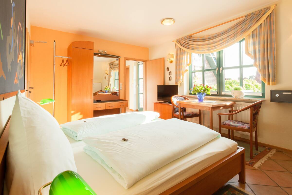 A hotel room with a bed, a desk, a chair, a TV, and a window with curtains.