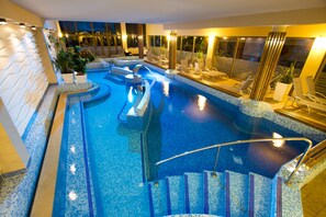 A large indoor swimming pool with multiple lanes, a seating area with chairs, and a staircase leading down to the pool.