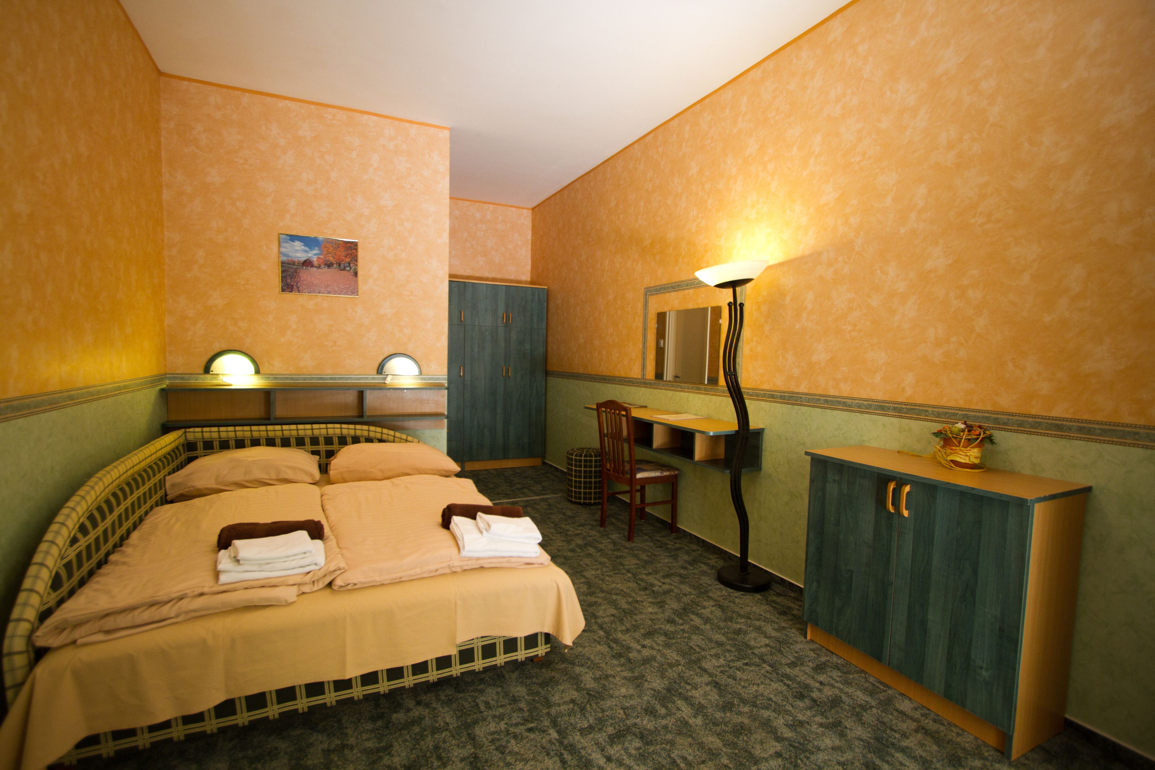 A hotel room with a bed, a desk, a chair, a wardrobe, and a lamp.