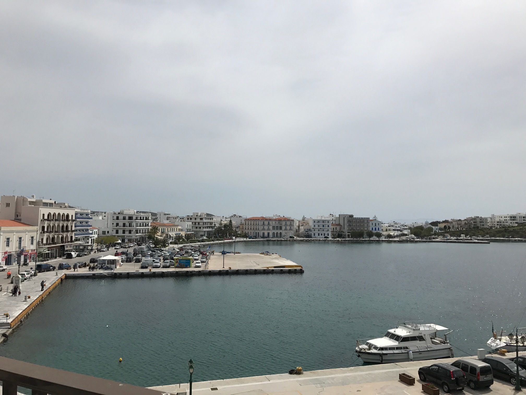 A waterfront area with buildings, a marina, and parked cars.