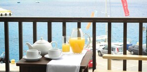 A table with a teapot, cups, and a glass of orange juice on a balcony overlooking the sea. - Hotel Lito (Tinos)