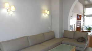 Un salon moderne avec un canapé d’angle beige, une table basse en verre et des luminaires fixés au mur.