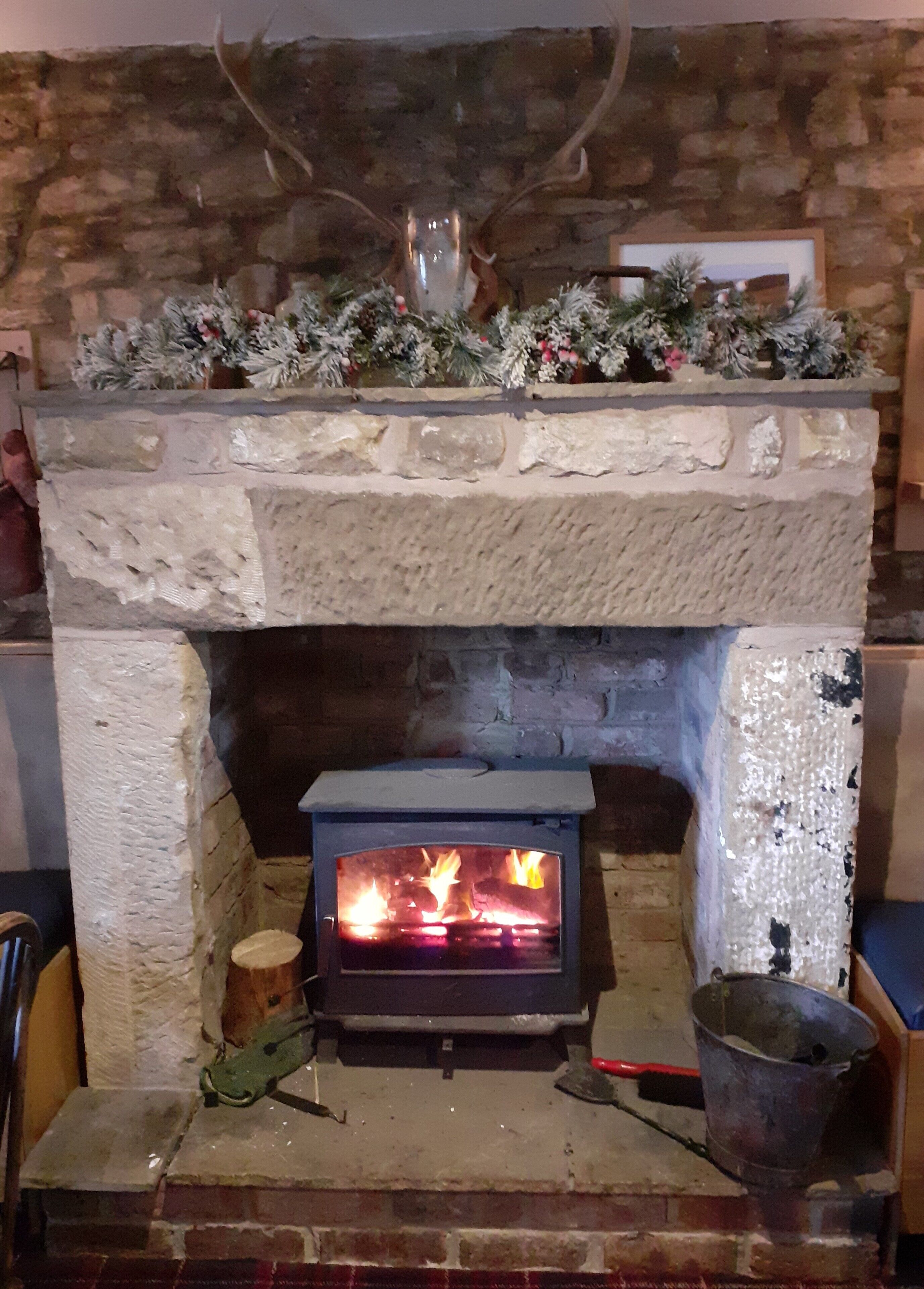 Una chimenea de piedra con estufa de leña, un fuste decorativo y una pared de piedra rústica.