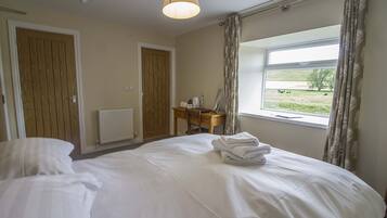 A hotel room with a bed, a desk with a chair, a window with curtains, and a view of the outdoors.
