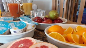 A breakfast table with various fruits, a pitcher of orange juice, and containers of yogurt.
