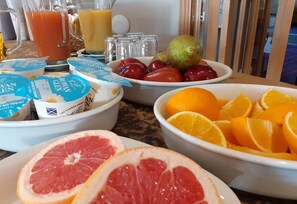 A breakfast table with various fruits, a pitcher of orange juice, and containers of yogurt.