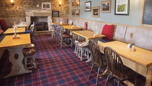 A restaurant interior with wooden tables and chairs, a stone wall, and framed pictures on the wall.