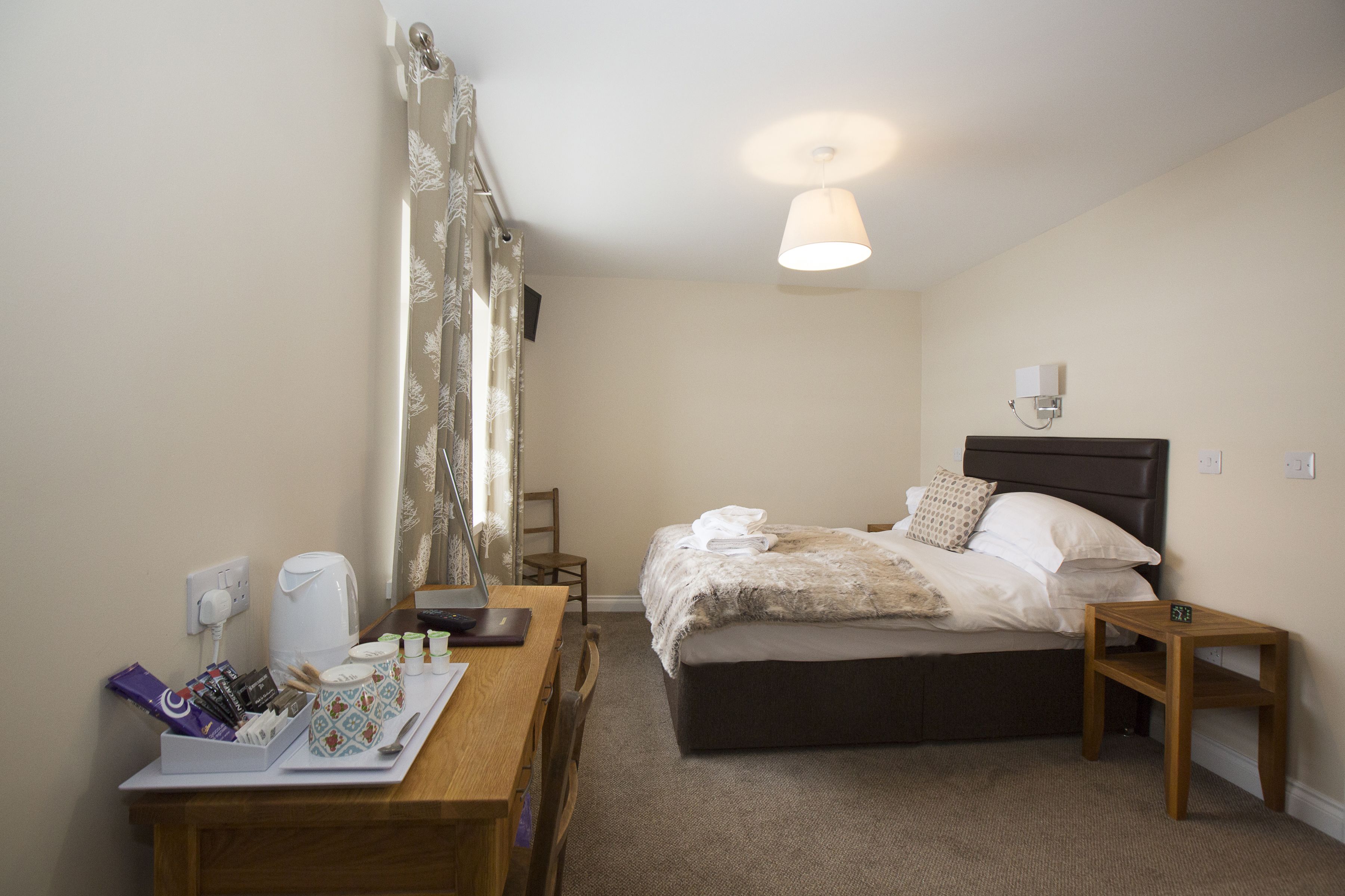 Une chambre d’hôtel comprenant un lit, une table de chevet, une chaise, un bureau avec un miroir et une lampe.