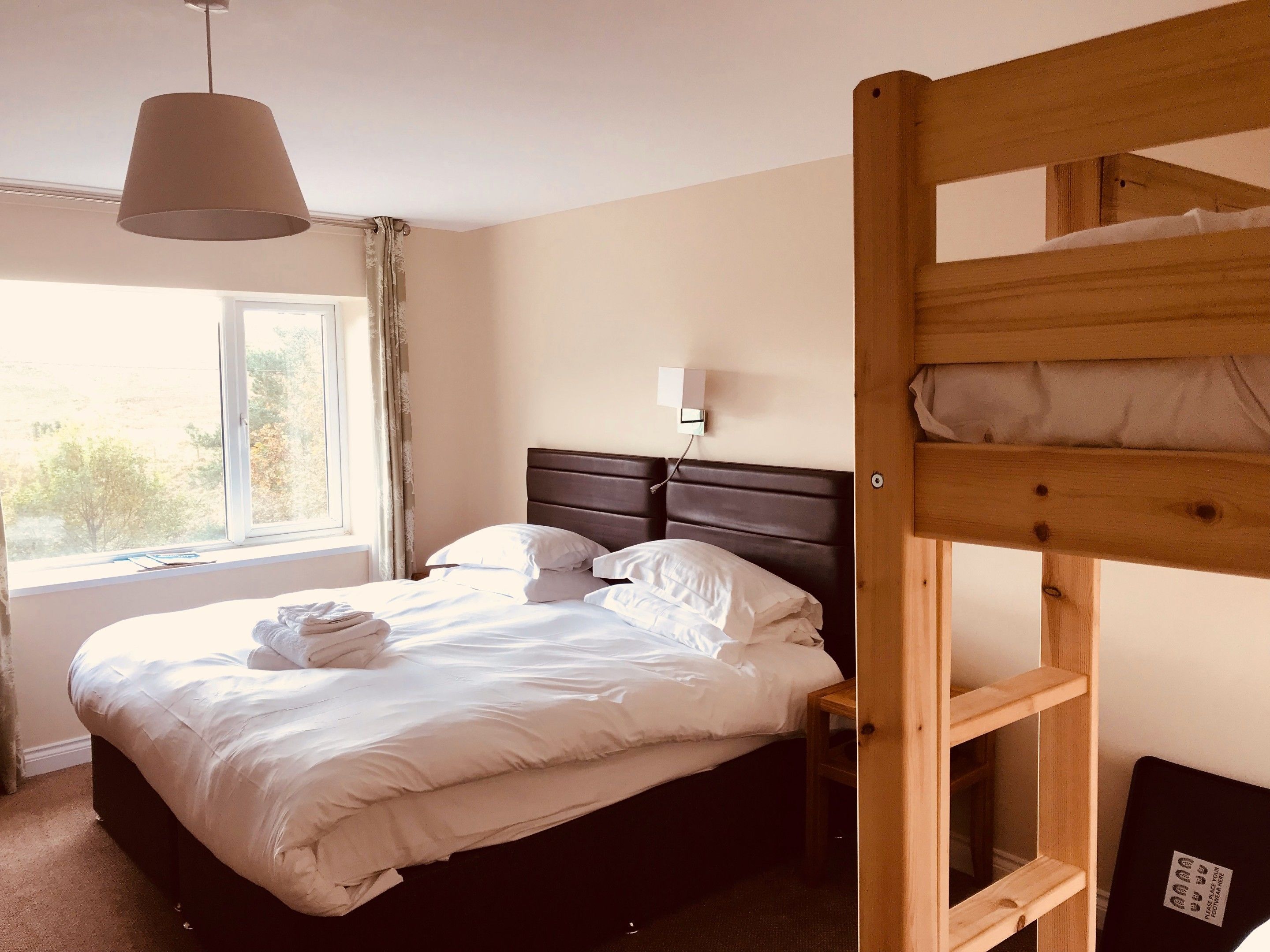 A single bed with a wooden headboard, a bedside table, a lamp, and a window with curtains.