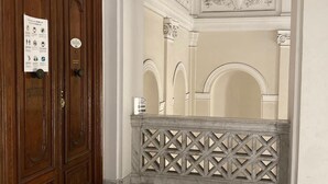 A hallway with a wooden door labeled "PIANO," a marble floor, and a decorative ceiling. - Piazza Bovio 22 (Naples)