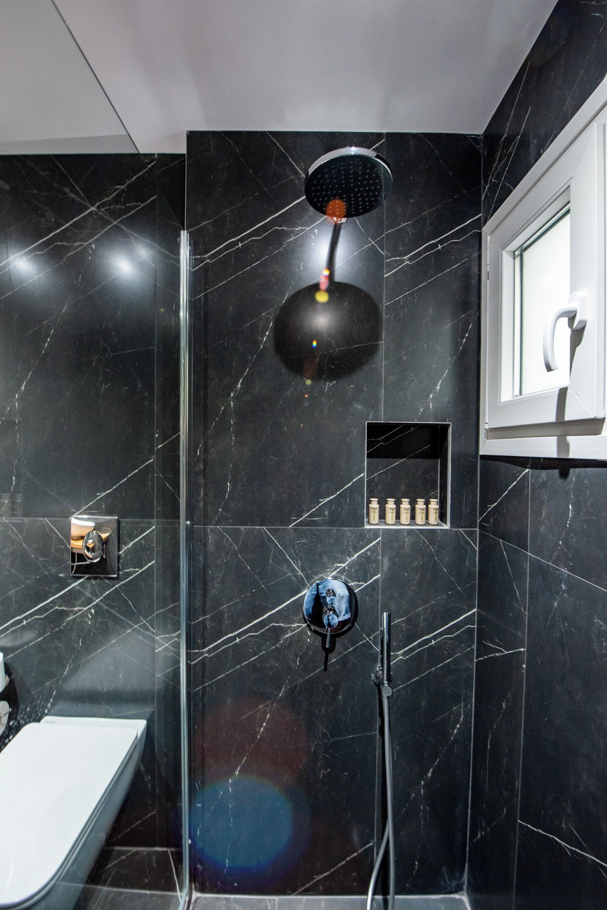 Ein modernes Badezimmer mit einer Duschkabine aus Glas, einer Handbrause und einem kleinen Ablagefach für Toilettenartikel.