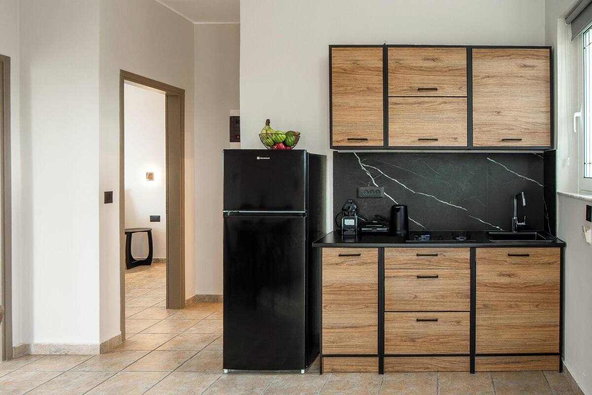 A modern kitchen with a black refrigerator, wooden cabinets, and a marble backsplash.