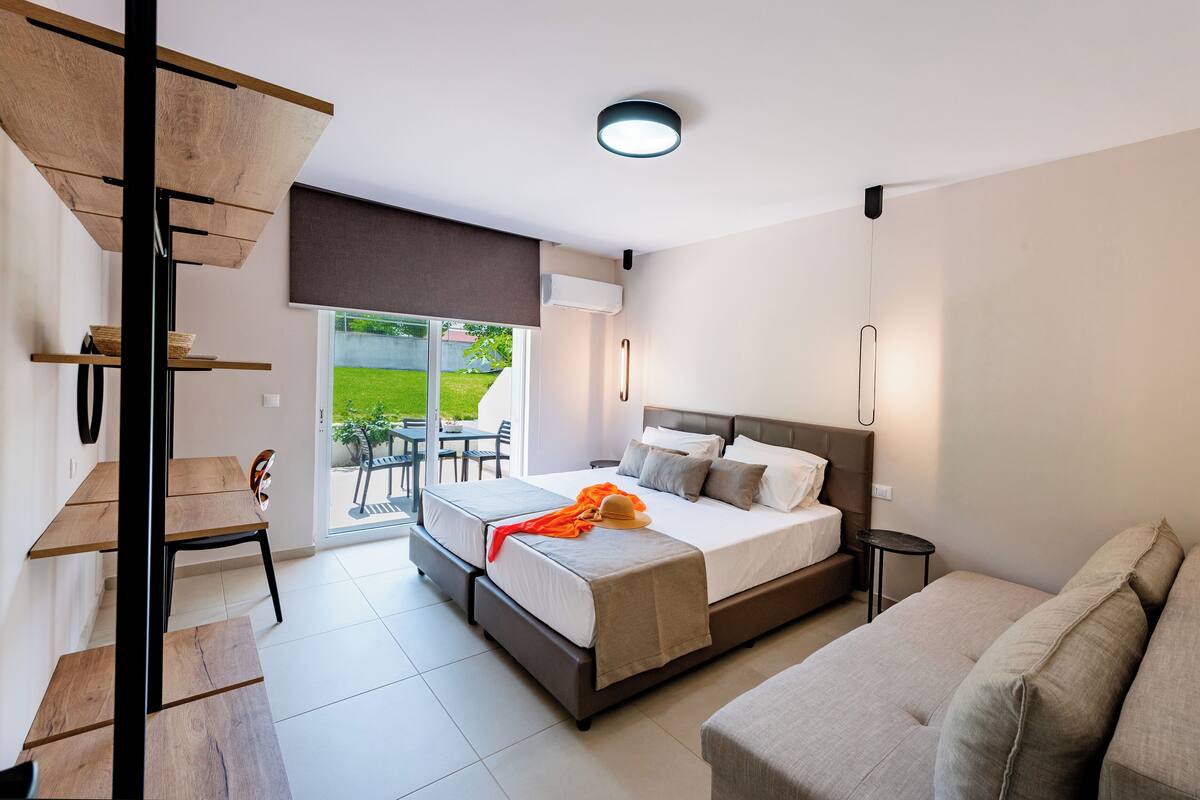 A modern bedroom with a bed, a sofa, a dining area with a table and chairs, and a staircase.