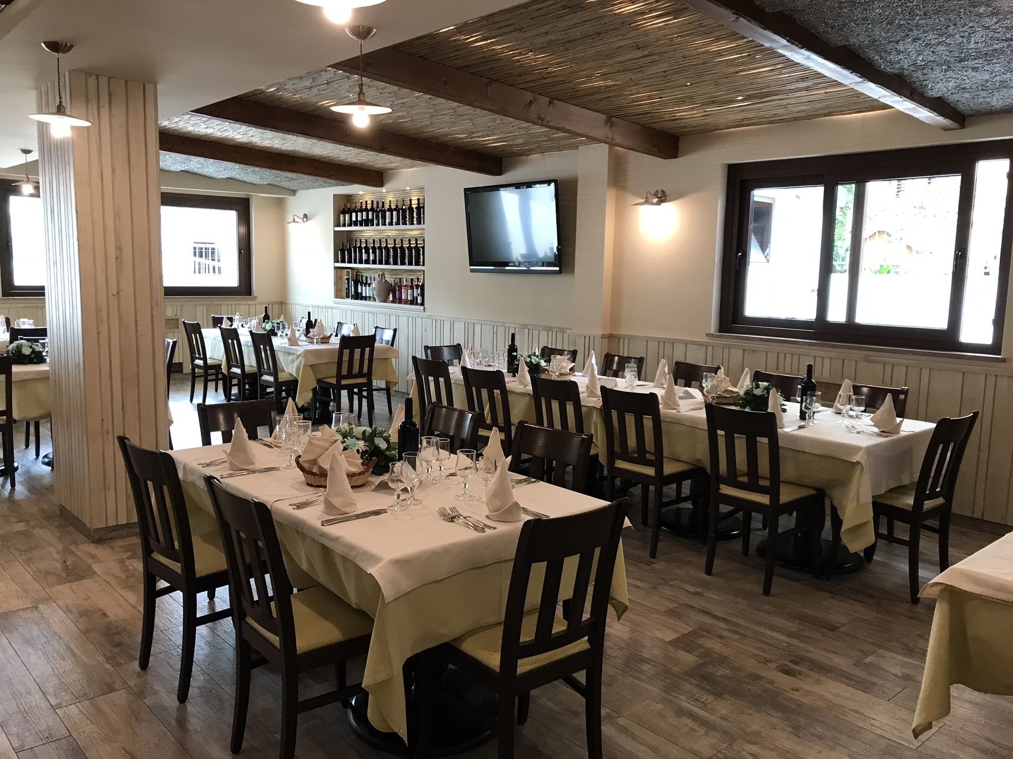 A restaurant with multiple tables set for dining, a television mounted on the wall, and a wine display.