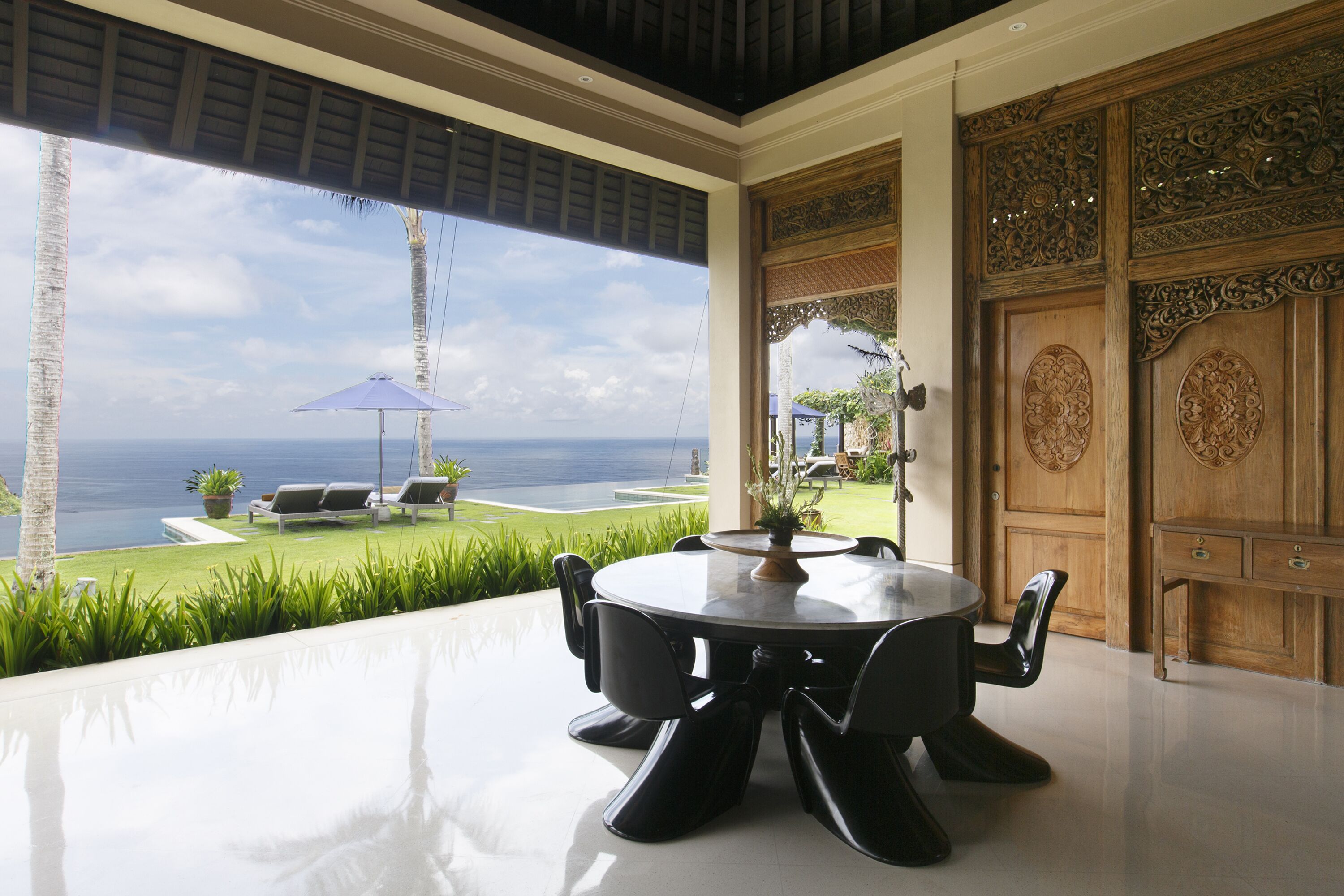 A modern dining area with a view of the ocean, a round table, and chairs.