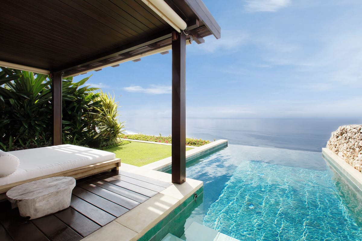 Ein privater Infinity-Pool mit Holzterrasse und weißer Liege.