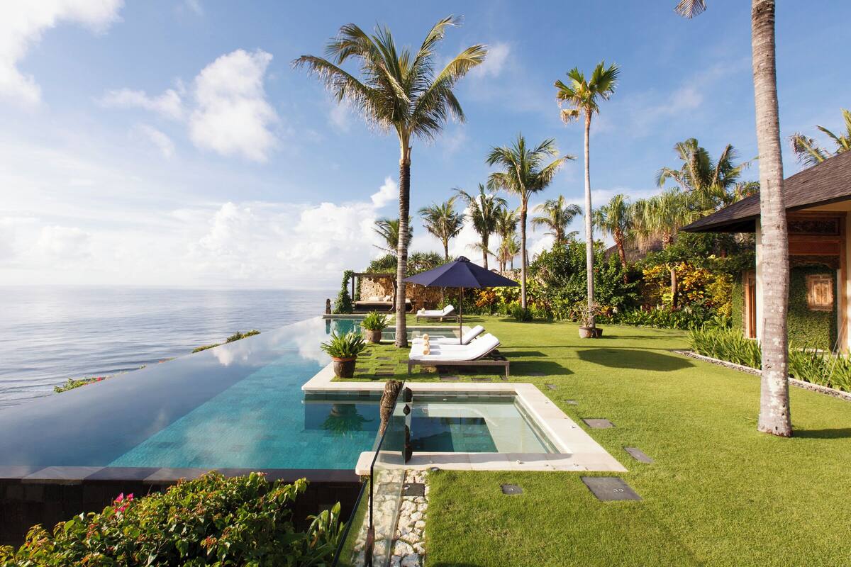 Ein luxuriöser Infinity-Pool mit freiem Blick auf den Ozean, umgeben von gepflegtem Rasen und Palmen.