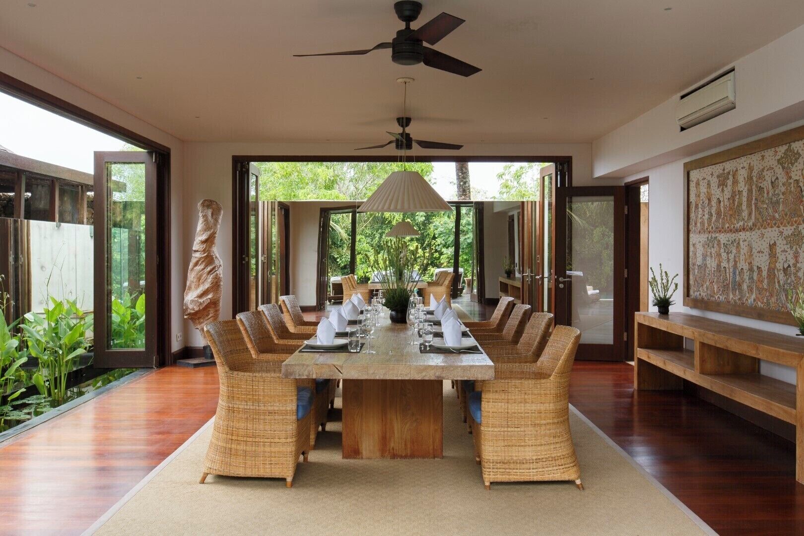A dining area with a large wooden table, wicker chairs, and a ceiling fan.