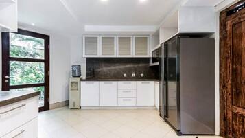 A modern kitchen with white cabinets, a black refrigerator, and a wooden door.