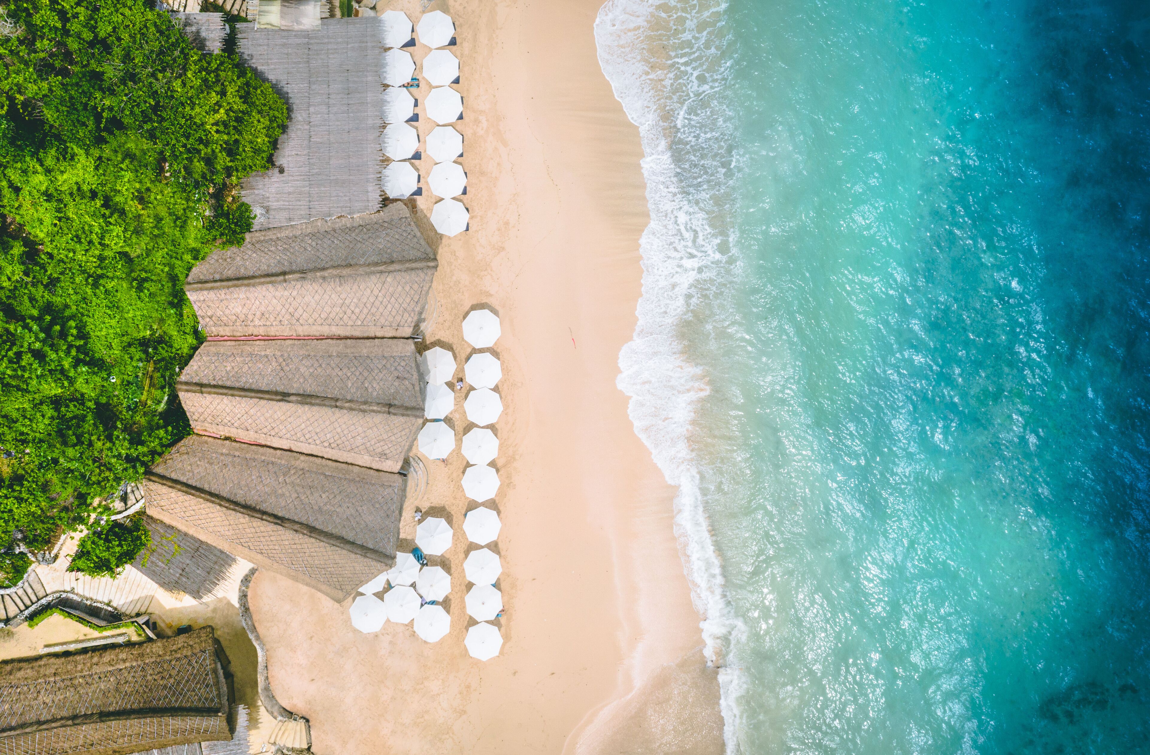 An aerial view of a beach with umbrellas and a paved walkway.