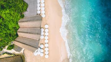 An aerial view of a beach with umbrellas and a paved walkway.