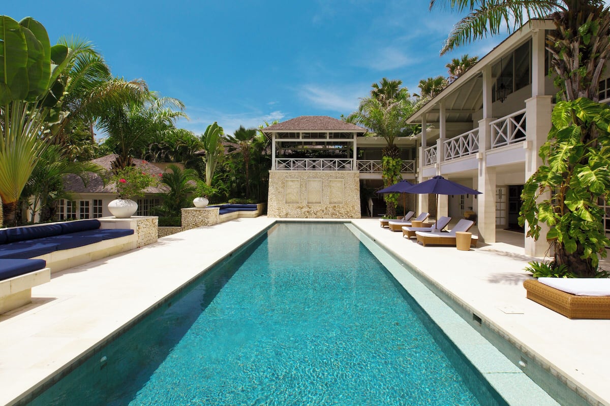 Ein Swimmingpool mit Liegestühlen und Sonnenschirmen, umgeben von Palmen und einem Gebäude mit Balkon.