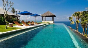 A pool with lounge chairs and umbrellas, a thatched-roof structure, and a view of the ocean. - The Ungasan Clifftop Resort (Pecatu)
