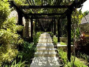 A stone pathway leading through a garden with a pergola structure. - The Ungasan Clifftop Resort (Pecatu)