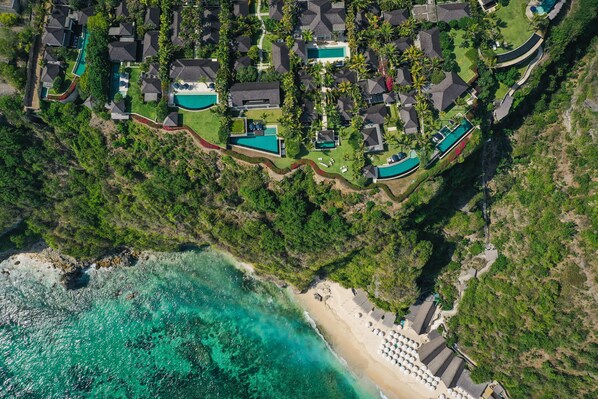 An aerial view of a coastal residential area with multiple houses, swimming pools, and a beach. - The Ungasan Clifftop Resort (Pecatu)