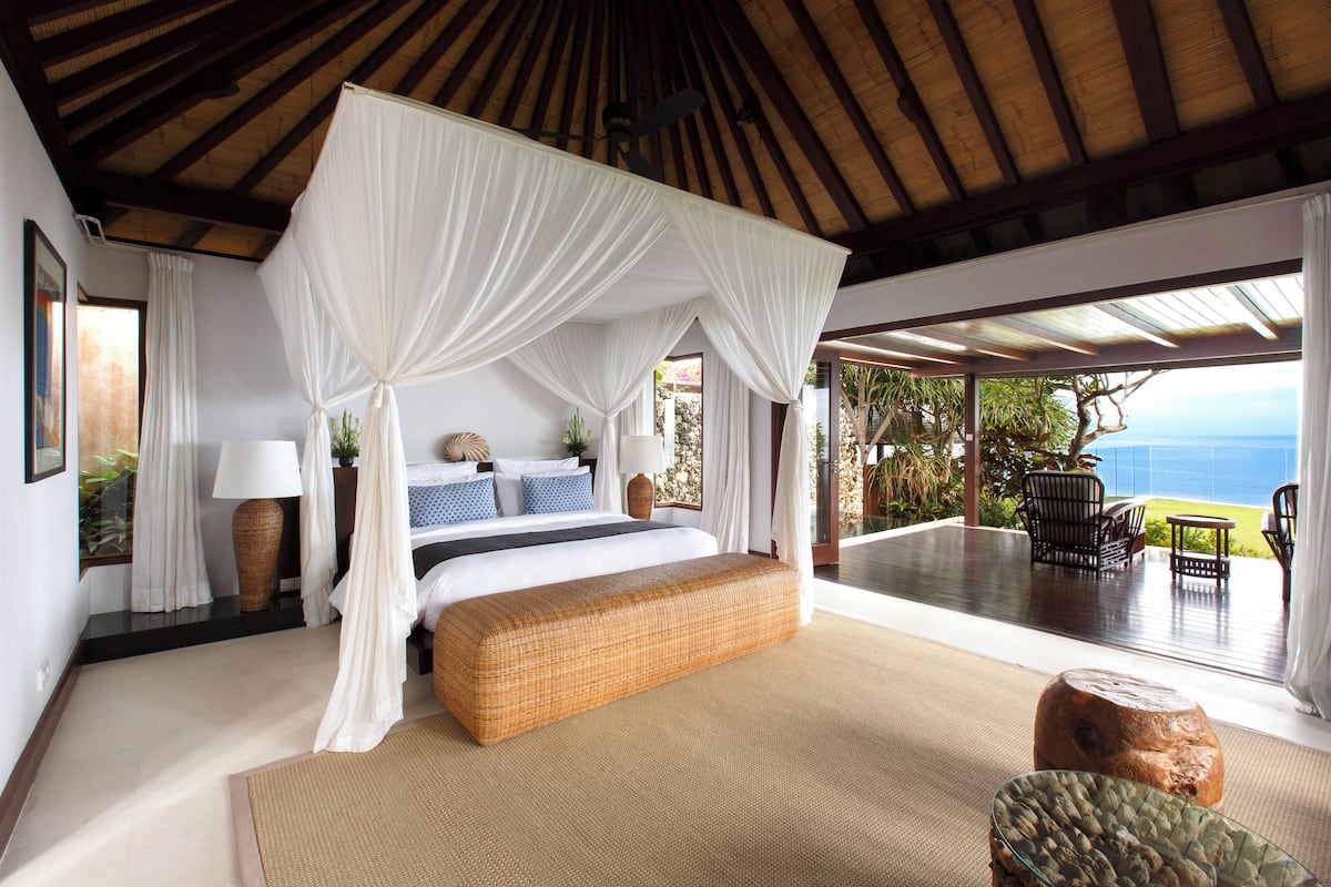 Ein Schlafzimmer mit Baldachinbett, großem Fenster und Meerblick.