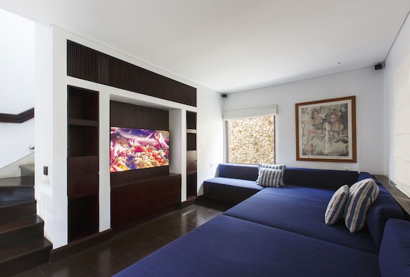 A modern living room with a large flat-screen TV, a blue sofa, and a staircase. - The Ungasan Clifftop Resort (Pecatu)