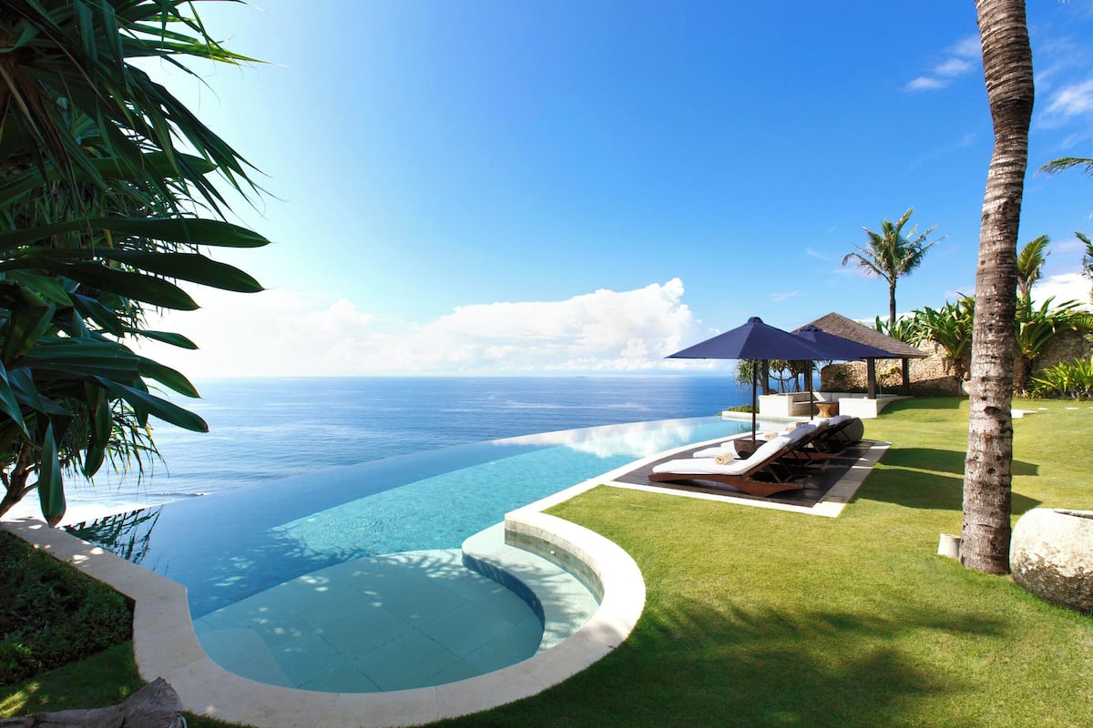 Ein Infinity-Pool mit Blick auf den Ozean, Liegestühle und Palmen.